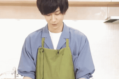 A Man Wearing A Green Apron And A Blue Shirt Is Cooking In A Kitchen GIF