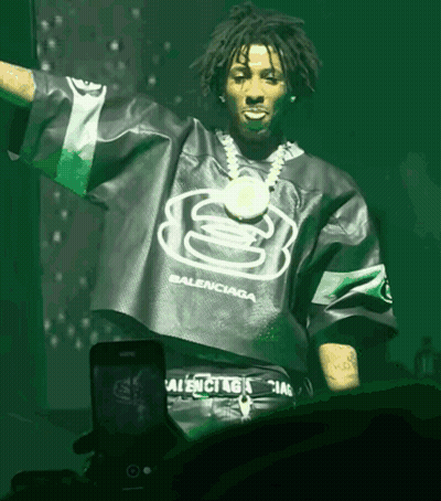 A Man Wearing A Green Balenciaga Shirt Stands In Front Of A Phone GIF