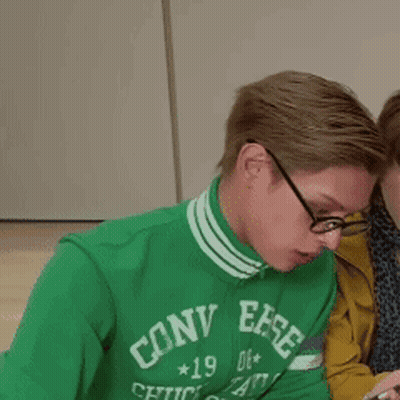 A Man Wearing A Green Converse Sweatshirt Looks At His Phone GIF