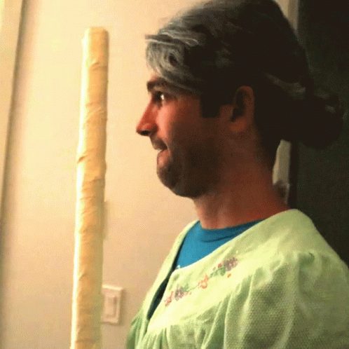 A Man Wearing A Green Dress And A Blue Shirt Stands In Front Of A Pole GIF