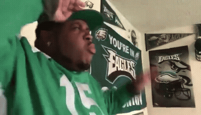 A Man Wearing A Green Eagles Jersey Is Standing In Front Of A Wall . GIF