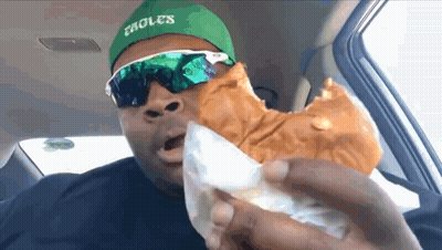 A Man Wearing A Green Hat And Sunglasses Is Eating A Sandwich . GIF