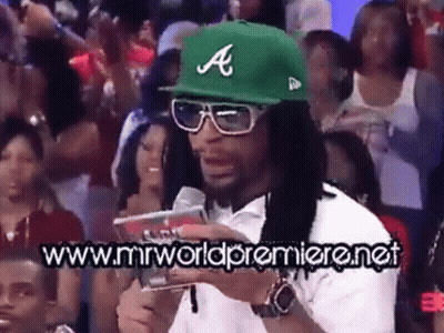 A Man Wearing A Green Hat With The Letter A On It Stands In Front Of A Crowd Of People GIF