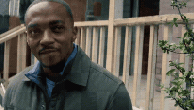 A Man Wearing A Green Jacket And A Blue Shirt Is Standing In Front Of A Railing GIF