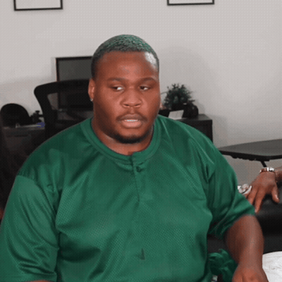 A Man Wearing A Green Nike Shirt Is Sitting At A Desk GIF
