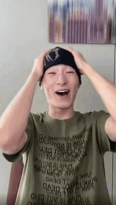 A Man Wearing A Green Shirt And A Black Beanie Is Laughing While Holding His Head . GIF