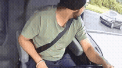 A Man Wearing A Green Shirt And A Black Hat Is Sitting In The Driver 'S Seat Of A Car GIF