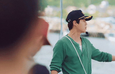 A Man Wearing A Green Shirt And A Black Hat With A Microphone Around His Neck Is Standing Next To A Woman . GIF
