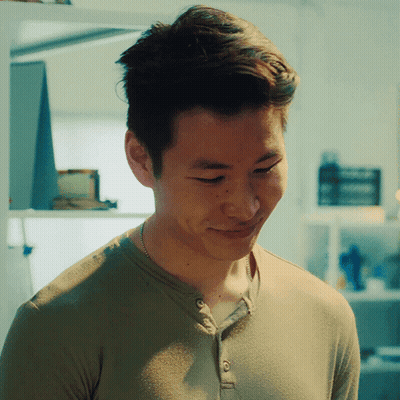 A Man Wearing A Green Shirt And A Necklace Smiles GIF