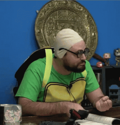 A Man Wearing A Green Shirt And A Yellow Vest Is Sitting At A Table With A Book Open . GIF