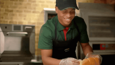 A Man Wearing A Green Shirt And Black Apron Is Smiling GIF