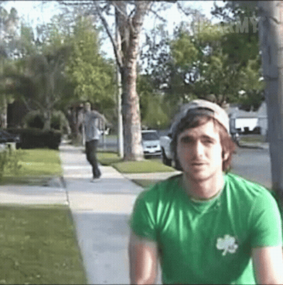 A Man Wearing A Green Shirt With A Shamrock On It Is Standing On A Sidewalk GIF