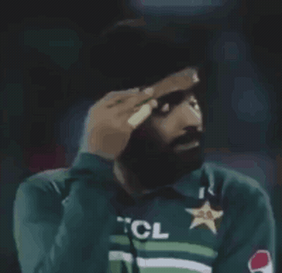 A Man Wearing A Green Shirt With A Star On It Is Covering His Face With His Hand . GIF