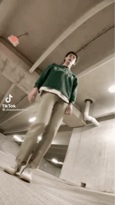 A Man Wearing A Green Sweater And Khaki Pants Is Standing In A Garage . GIF