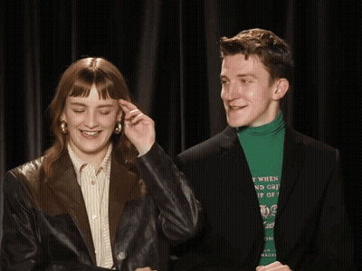 A Man Wearing A Green Turtleneck Is Standing Next To A Woman GIF