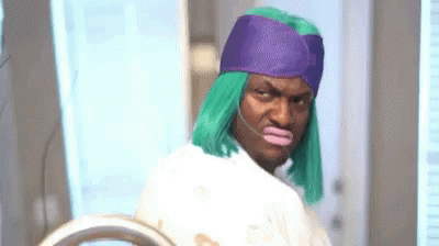 A Man Wearing A Green Wig And A Purple Hat Is Standing In Front Of A Mirror . GIF