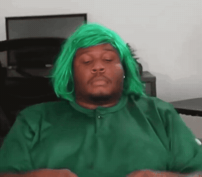 A Man Wearing A Green Wig Is Sitting At A Desk With His Eyes Closed . GIF