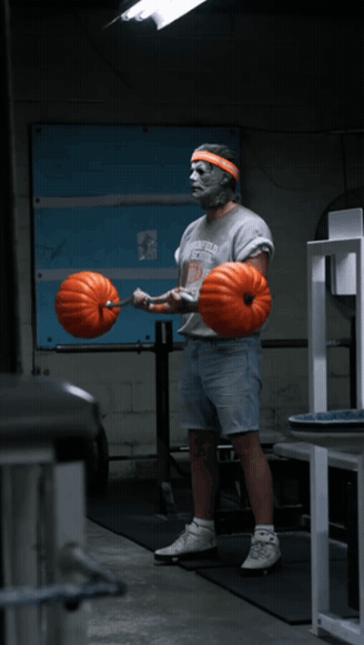 A Man Wearing A Greenfield School Shirt Is Lifting A Barbell With Pumpkins On It GIF