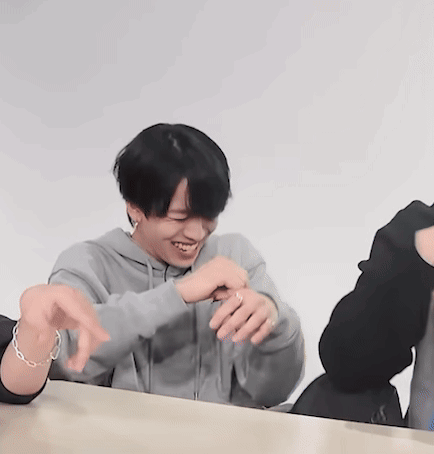 A Man Wearing A Grey Hoodie Is Sitting At A Table With His Hands Outstretched GIF