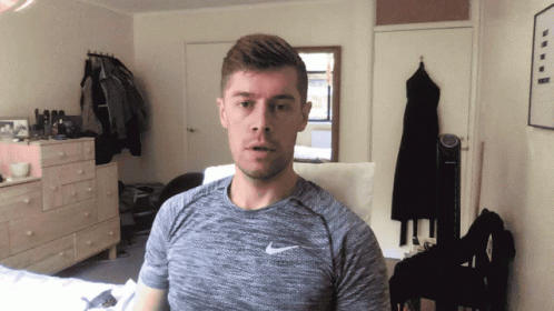 A Man Wearing A Grey Nike Shirt Is Standing In A Bedroom GIF