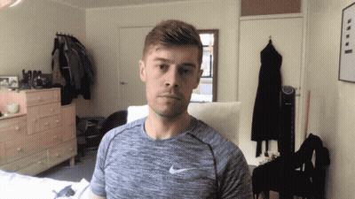 A Man Wearing A Grey Nike Shirt Stands In A Room GIF