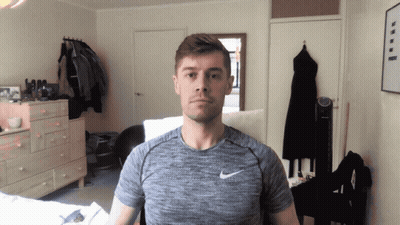 A Man Wearing A Grey Nike Shirt Stands In A Room GIF