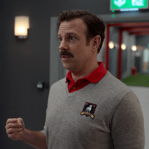 A Man Wearing A Grey Sweater And A Red Shirt Has The Word Yuck On His Shirt GIF