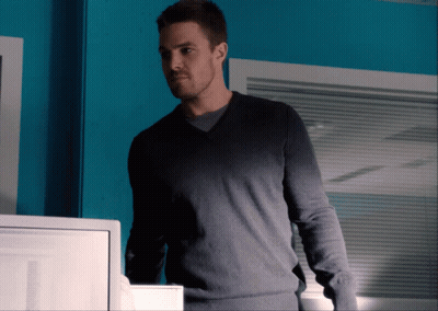 A Man Wearing A Grey Sweater Stands In Front Of A Blue Wall GIF