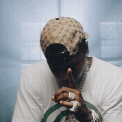 A Man Wearing A Gucci Hat Is Covering His Mouth With His Hand GIF