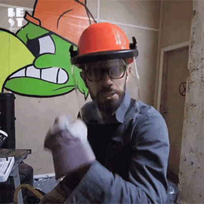 A Man Wearing A Hard Hat And Gloves Is Standing In Front Of A Wall That Has Graffiti On It GIF
