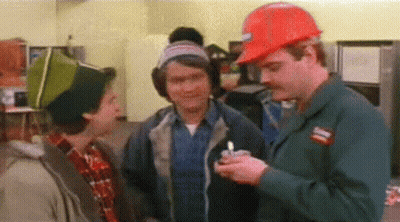 A Man Wearing A Hard Hat Is Holding A Lighter And Talking To Two Other Men In A Kitchen . GIF