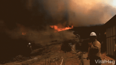 A Man Wearing A Hard Hat Stands In Front Of A Fire With The Words Viralhog Written On The Bottom GIF