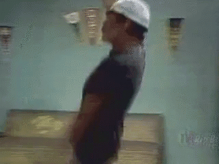 A Man Wearing A Hat And A Black Shirt Is Standing On A Bed . GIF
