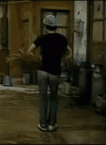 A Man Wearing A Hat And A Black Shirt Is Walking Down A Muddy Street GIF