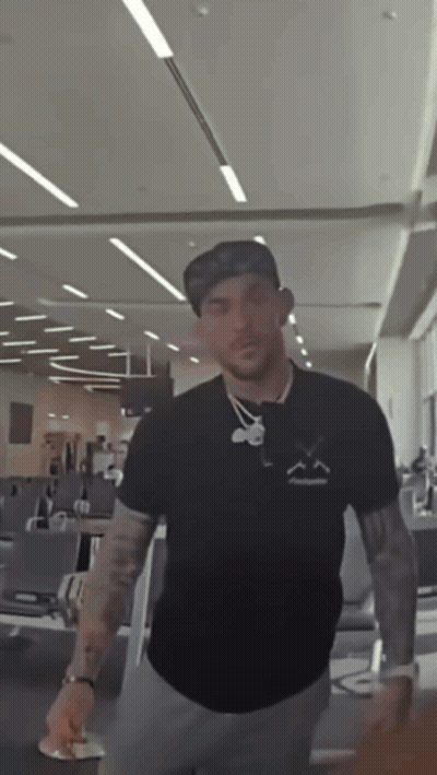 A Man Wearing A Hat And A Black Shirt With A Smiley Face On It GIF