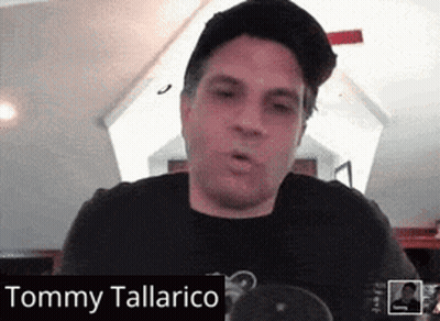 A Man Wearing A Hat And A Black Shirt With The Name Tommy Tallarico On The Bottom GIF