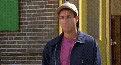 A Man Wearing A Hat And A Blue Jacket Is Standing In Front Of A Brick Building . GIF
