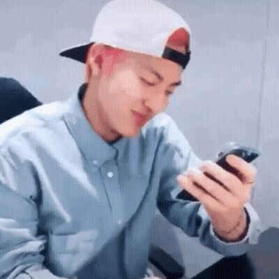 A Man Wearing A Hat And A Blue Shirt Is Looking At His Phone . GIF