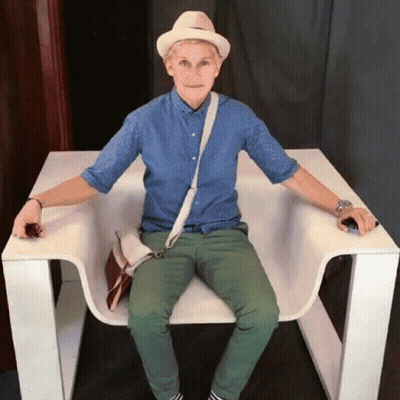 A Man Wearing A Hat And A Blue Shirt Is Sitting In A White Chair GIF