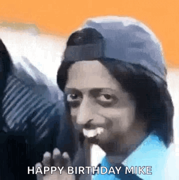 A Man Wearing A Hat And A Blue Shirt Is Smiling And Waving At The Camera . GIF
