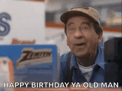A Man Wearing A Hat And A Blue Shirt Is Standing In Front Of A Sign That Says Happy Birthday Ya Old Man . GIF