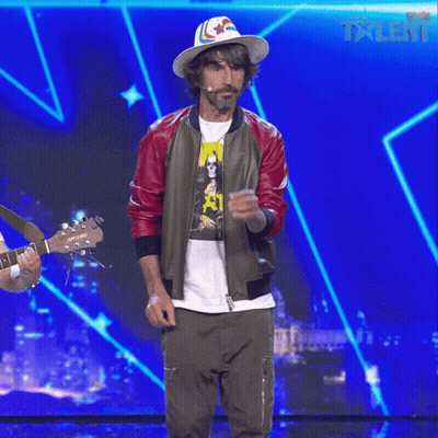 A Man Wearing A Hat And A Bomber Jacket Stands On A Stage With A Blue Background That Says Talent GIF