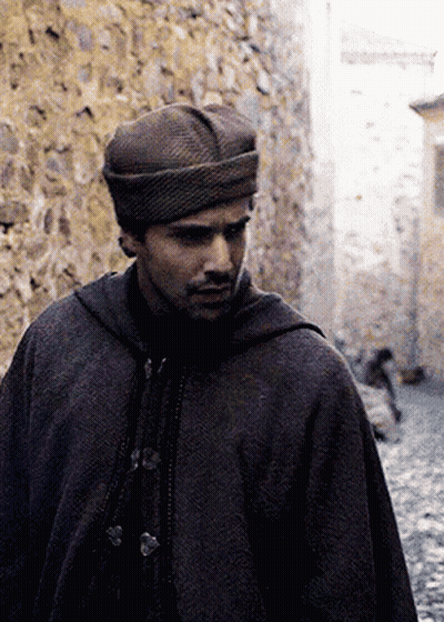 a man wearing a hat and a cape is walking down a narrow street