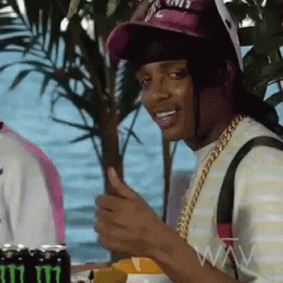 A Man Wearing A Hat And A Chain Is Giving A Thumbs Up Sign . GIF