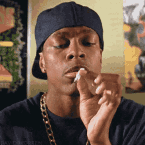 A Man Wearing A Hat And A Chain Is Smoking A Cigarette .. GIF