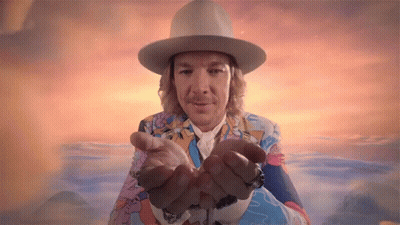 A Man Wearing A Hat And A Colorful Suit Is Holding His Hands Out GIF