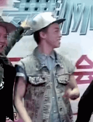 A Man Wearing A Hat And A Denim Vest Is Standing In Front Of A Sign That Says ' A ' On It GIF