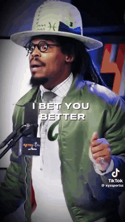 A Man Wearing A Hat And A Green Jacket Stands In Front Of A Microphone And Says I Bet You Better GIF