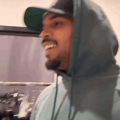 A Man Wearing A Hat And A Hoodie Is Smiling In A Kitchen . GIF
