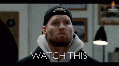 A Man Wearing A Hat And A Hoodie With The Words Watch This Below Him GIF